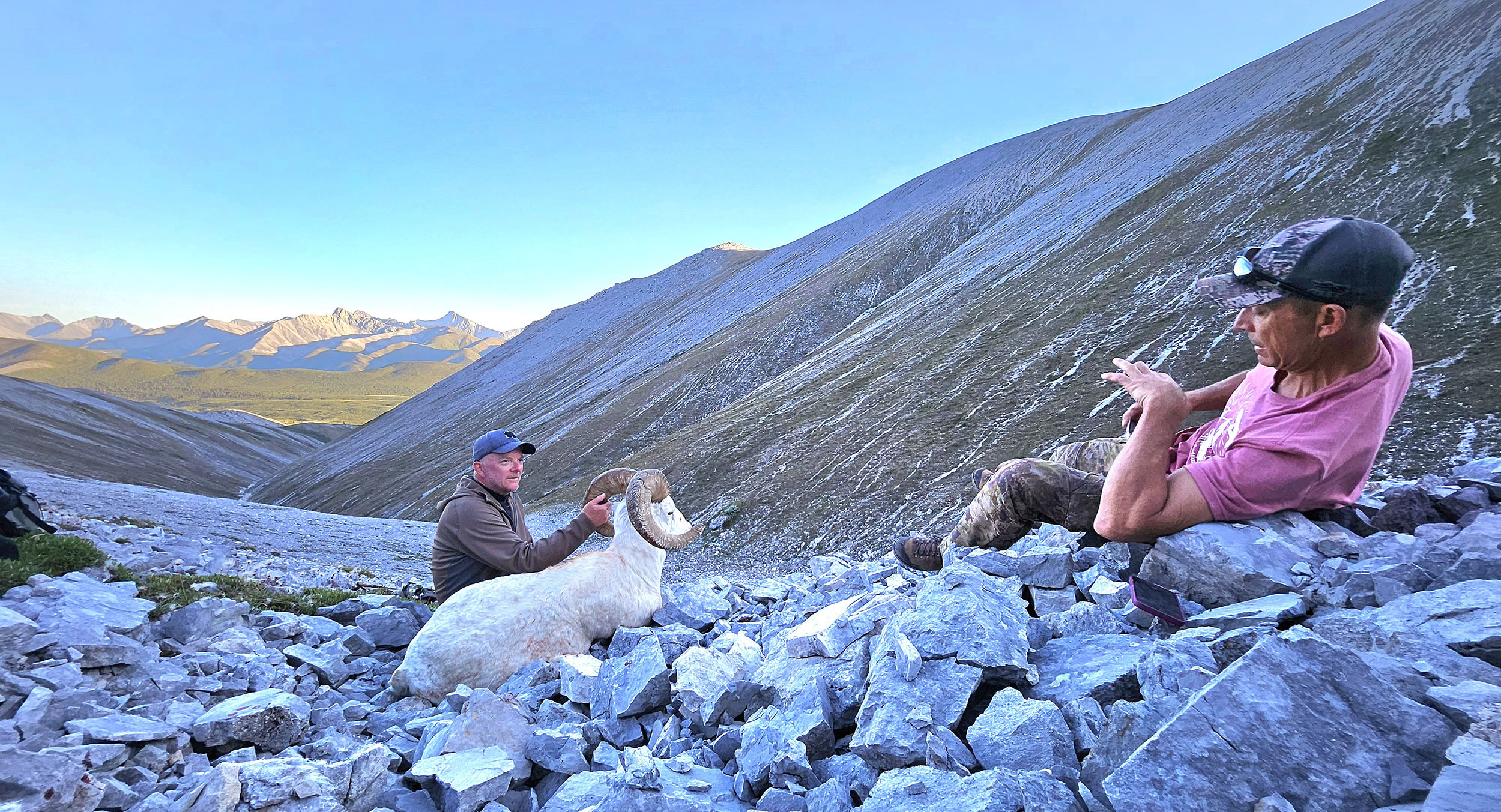 Guide taking a photo of a hunter with his ram on a mountainside