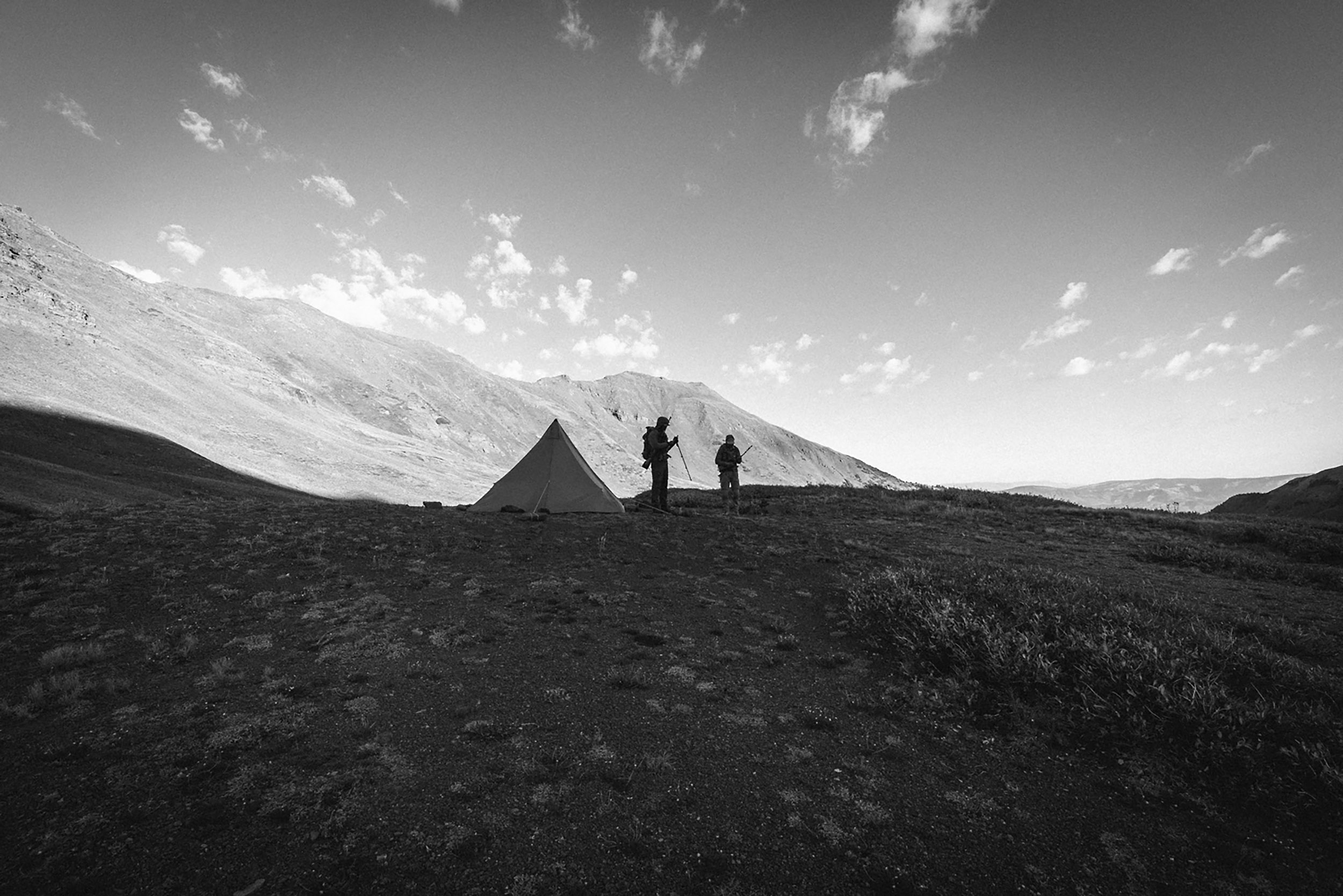 Silhouette of hunters by their tents on a ridge by Kelby Fassiotto