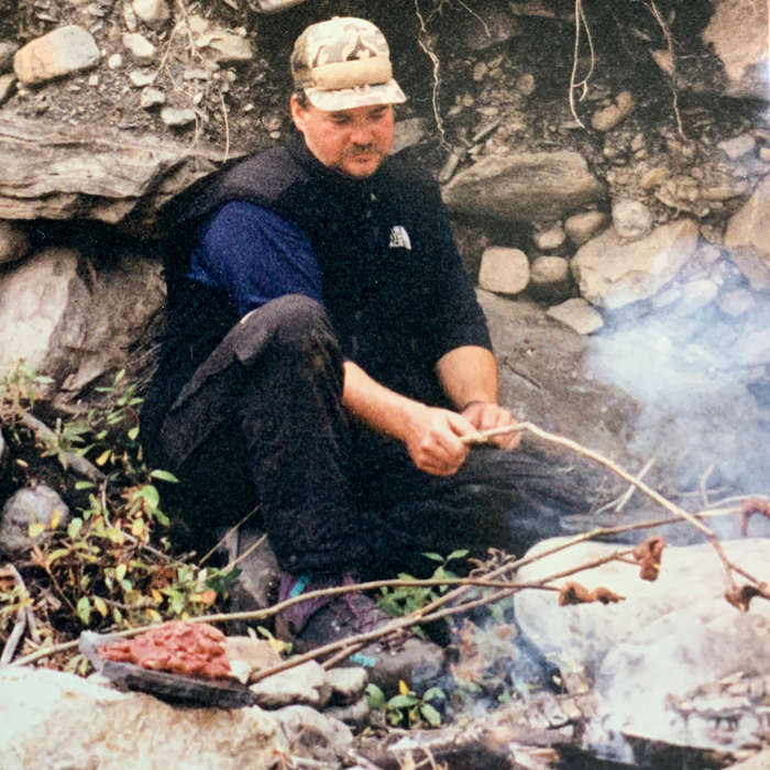 Man cooking meat over a primitive camp fire